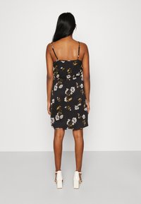 Czarna sukienka letnia w kwiaty z cienkimi ramiączkami, elastyczną talią i długością do kolan. Materiał ma lekki, zwiewny teksturę z białymi i żółtymi kwiatami.