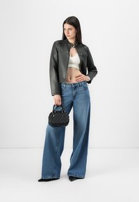 Černá kožená bunda s límečkem, světle zbarvený crop top a široké světle modré džíny. Drží texturovanou černou kabelku.