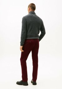 Donkergrijze, textuurgegeven, hoogsluitende trui gecombineerd met bordeaux corduroybroek, met een getailleerde snit en zwarte instappers.