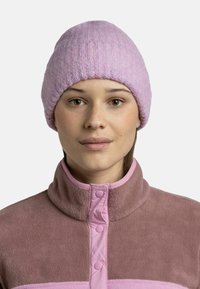 Gorra de punto de color púrpura claro con textura acanalada, que ofrece un ajuste ceñido. Combinada con una chaqueta de forro polar marrón con detalles y botones en rosa.