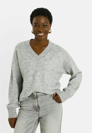 Pull gris à col en V avec poignets et ourlet côtelés, présentant une coupe décontractée et une texture douce, associé à un jean gris clair.