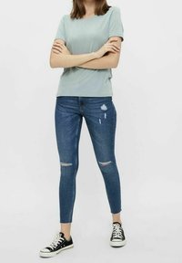 Top corto de color verde claro con mangas cortas, jeans ajustados azules con detalles desgastados y zapatillas negras. Silueta relajada pero ajustada.