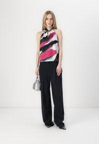 Halterneck-Top mit einem bunten abstrakten Muster in Pink, Schwarz und Weiß, kombiniert mit navyblauen weit geschnittenen Hosen und einer silbernen Handtasche.