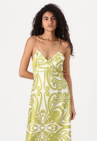 Vestido com alças spaghetti, em verde e branco com padrão, apresentando um decote em V profundo e uma silhueta fluida, com uma textura ligeiramente brilhante.