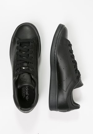 Black leather sneakers with a smooth finish, round toe, flat rubber sole, and contrasting stitching. Features five eyelets and perforated details.