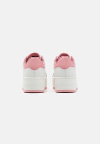 White sneakers with pink accents and textured heel. Features a thick white platform sole. Brand logo displayed on the side.