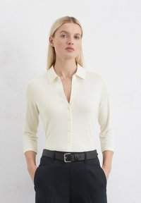Linen blend, light ivory blouse with a collared neckline and six button placket. Features three-quarter sleeves and smooth texture.