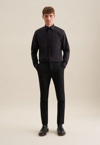 Zwart op maat gemaakt shirt met een klassieke kraag, knoopsluiting aan de voorkant en lange mouwen, gecombineerd met zwarte slim-fit broeken en zwarte leren schoenen.