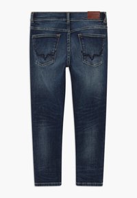 Vaqueros de mezclilla azul oscuro con una textura suave, que cuentan con dos bolsillos traseros y un parche de logo sutil. Diseño de pierna recta.