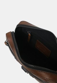 Borsa in pelle marrone con chiusura a zip, dotata di fodera interna nera, piccola tasca con zip e un'etichetta in pelle all'interno.