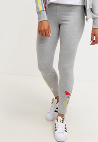 Grå leggings med en tajt passform, gjorda av mjukt material, med färgglada varumärkeslogotyper i gul, röd och blå nyanser vid anklarna.