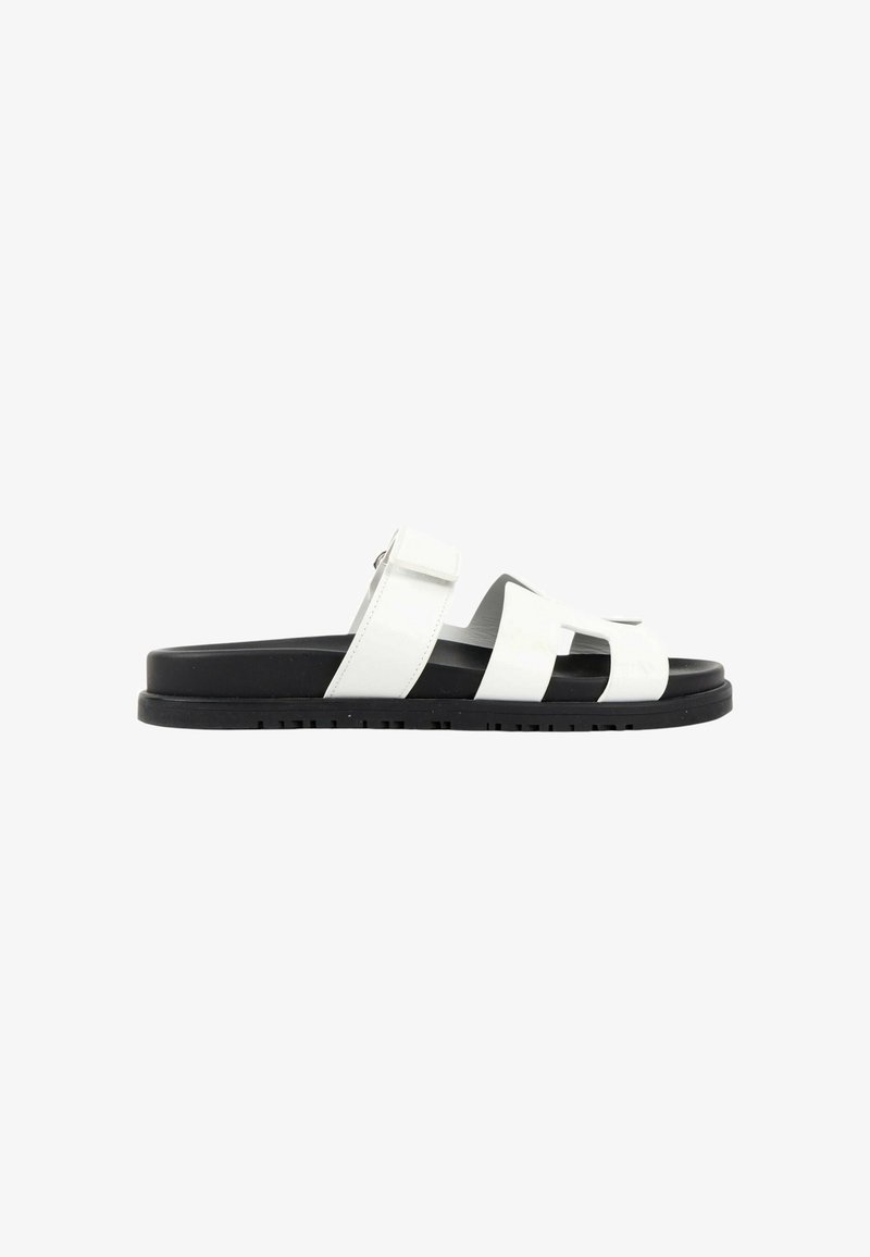 Sandale blanche homme à bout ouvert avec semelle noire et bride ajustable sur fond blanc uni.