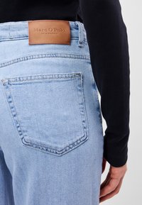 Ανοιχτό μπλε τζιν παντελόνι με ευθεία γραμμή, που διαθέτει καφέ δερμάτινη ετικέτα στον πάνα και μια πίσω τσέπη με ραμμένα σ�χέδια.