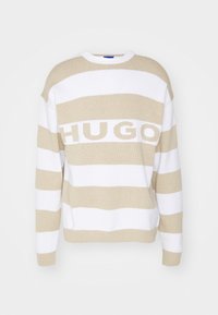 Pull rayé beige et blanc en tricot doux, avec un col rond large et le texte "HUGO" au centre. Coupe ample avec des épaules tombantes.