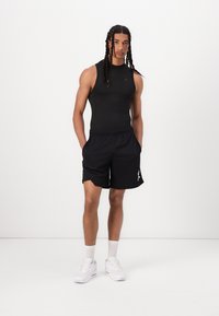 Top deportivo negro sin mangas y pantalones cortos negros con una cintura elástica. Zapatillas blancas y calcetines tobilleros blancos. Diseño simple, aspecto deportivo.