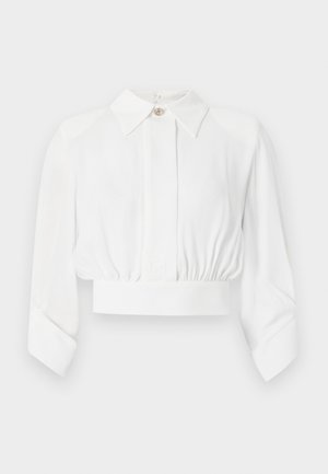 Bluza albă cropată cu mâneci lungi, guler ascuțit, nasturi frontali ascunși, talie elastică și manșete largi.