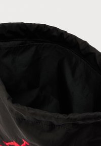 Μαύρη τσάντα με σούρωμα στην πάνω άκρη, κατασκευασμένη από λείο ύφασμα. Το εσωτερικό είναι ευρύχωρο, με απαλό, αδιαφανές υλικό και χωρίς επιπλέον διακοσμητικά στοιχεία.