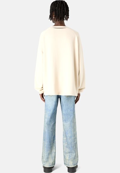 Hellbeige übergroßer Strickpullover mit überschnittenen Schultern, kombiniert mit verblassten blauen weit geschnittenen Jeans. Das Outfit zeichnet sich durch ein minimalistisches Design aus.