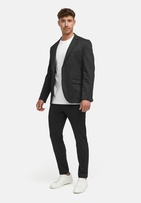 Grå blazer med en rad knappar, bärs över en vit t-shirt; kombineras med svarta byxor och vita sneakers.