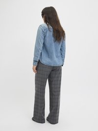 Denimskjorte med lange ermer, lyseblå farge og knappedetaljer; kombinert med høytlivede grå rutete bukser i vid ben.