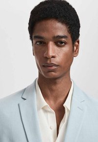 Jasnoniebieska marynarka na białej koszuli, z klapami w kształcie łezki i pojedynczym guzikiem, o gładkiej fakturze i minimalistycznym designie.