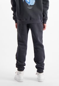Zwarte sweatshirt met een blauwe grafiek op de achterkant, gecombineerd met bijpassende zwarte joggingbroek met elastische mouwen, gedragen met witte sneakers.