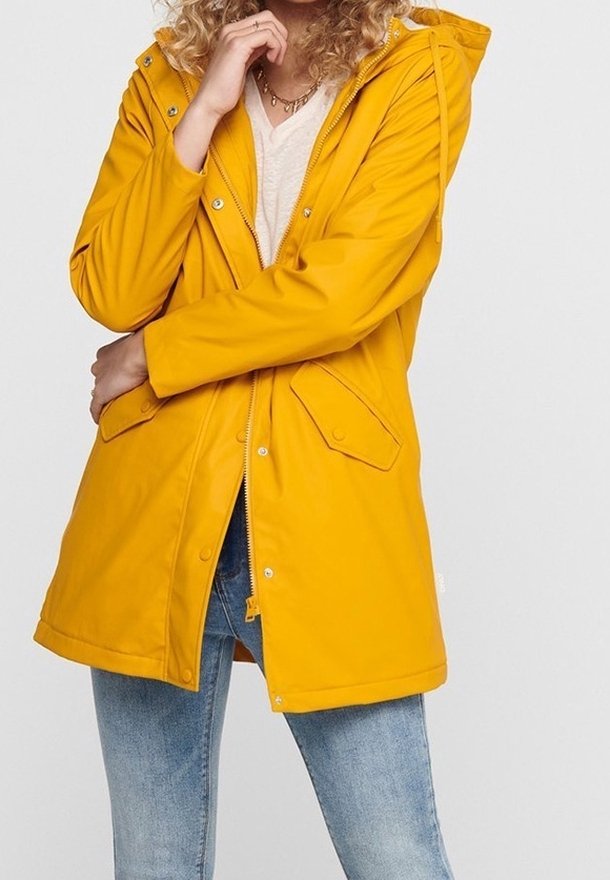 Imperméable jaune avec capuche, fermeture éclair frontale, poches à boutons-pression, et design longueur genou, assorti à un jean bleu clair.