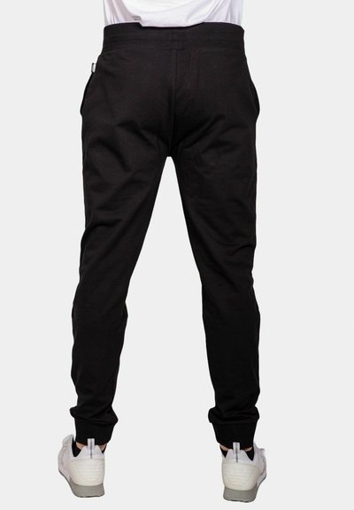 Pantaloni sportivi neri con una vestibilità affusolata, dotati di tasche laterali e cintura elastica. Indossati con sneakers bianche. Texture liscia.