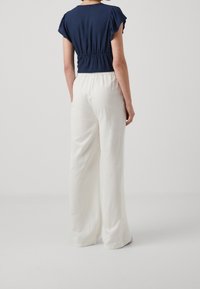 Navy blue short-sleeve top with gathered waist, paired with loose-fitting white trousers in a light fabric, featuring a smooth texture.