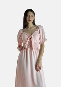 Rosa Kleid mit kurzen Puffärmeln und einem gebundenen Ausschnitt. Das Oberteil hat eine smockierte Verarbeitung und geht in einen weiten Rock über, der eine weiche Textur aufweist.