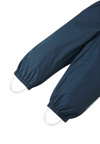 Pantaloni impermeabili blu navy con polsini elastici e dettagli bianchi. Presentano una tasca laterale e una superficie liscia e lucida.