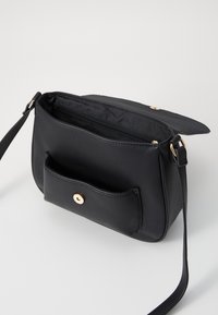 Sac bandoulière en cuir noir avec une finition texturée, quincaillerie dorée, intérieur zippé et une poche externe avec fermeture à snap.