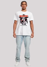 White cotton t-shirt featuring red and black "Beastie Boys" graphic, paired with light blue denim jeans and white sneakers.