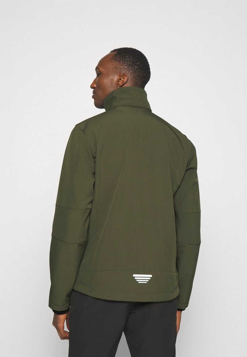 Chaqueta verde con un alto cuello, que presenta una textura suave, puños negros contrastantes y un detalle triangular reflectante en el dobladillo trasero.