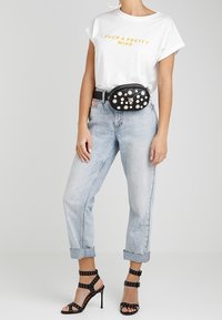 Persona che indossa una maglietta bianca con la scritta "Such a Pretty Mind", jeans azzurri arrotolati, borsa a tracolla nera con borchie e sandali neri con tacco alto e borchie.