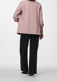 Světle růžový blazer s třičtvrtinovými rukávy, zadním rozparkem, nošený přes černé kalhoty s širokými nohavicemi a černé tenisky s bílou podrážkou.