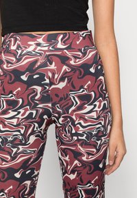 Leggings de cintura alta com um padrão em espiral nas cores bordô, preto e creme. Textura suave com um ajuste justo e um cós elástico.