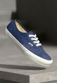 Blue suede low-top sneaker with white laces and rubber sole. Features a branded tag on the side and a smooth upper texture.