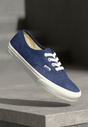 Blue suede low-top sneaker with white laces and rubber sole. Features a branded tag on the side and a smooth upper texture.