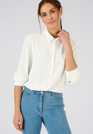 White button-up shirt with a collar, long sleeves, and buttons down the front, paired with light blue denim jeans.