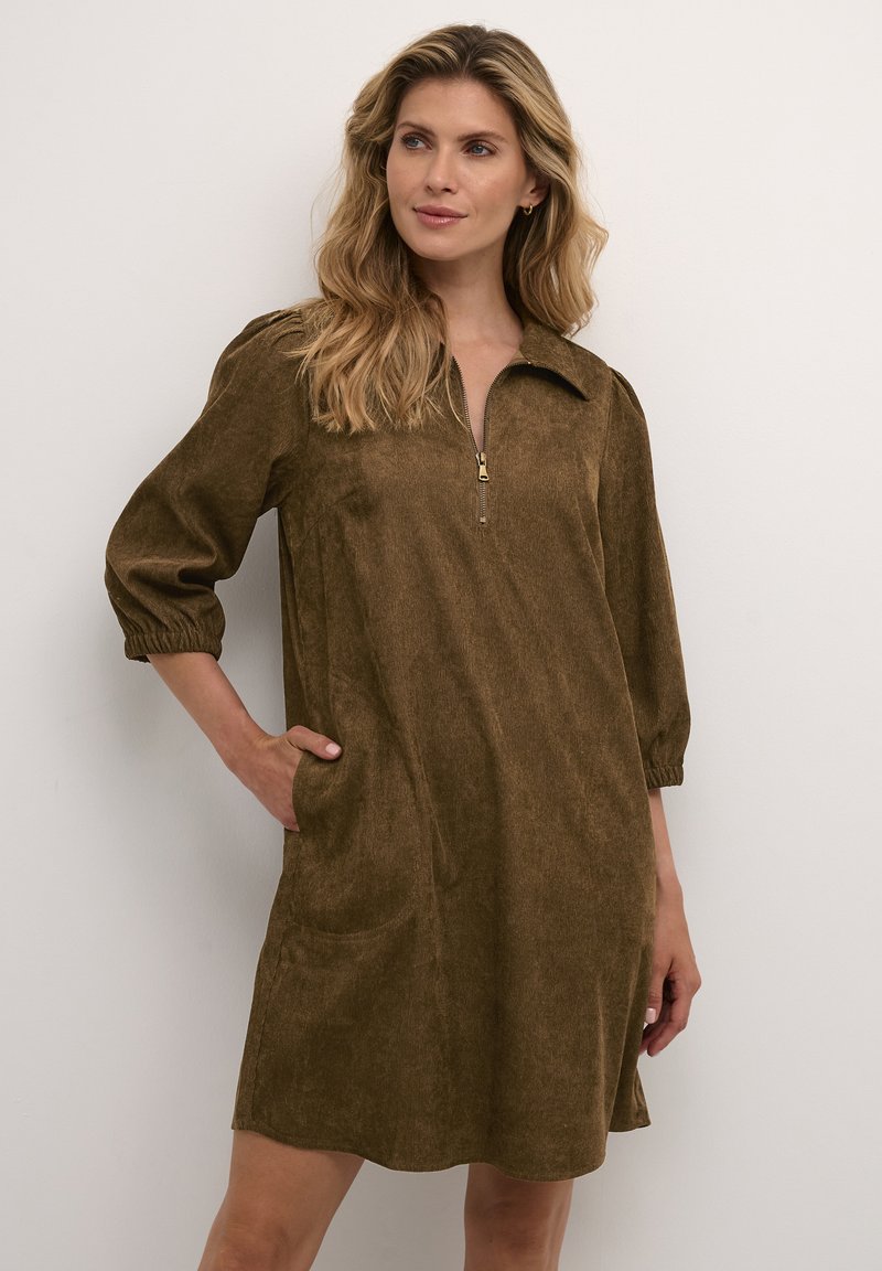 Abito in corduroy marrone con colletto a metà zip, maniche a tre quarti e tasche; texture morbida con una silhouette leggermente svasata.