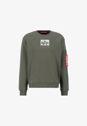 Olivno zelena kapuca iz mešanice bombaža. Ima bel logo na prsih in žep na rokavu z zadrgo ter rdečo etiketo. Ribičasti manšeti in rob.