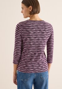 Top a righe viola e rosa con scollatura arrotondata e maniche a tre quarti. Realizzato in un tessuto testurizzato, abbinato a jeans in denim blu.