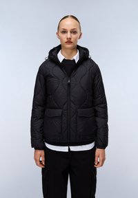 Svart quiltad puffjacka med huva, frontdragkedja och tv�å stora fickor. Har en slät yta och elastisk nederkant, lager på lager över en vit skjorta.