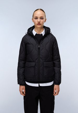 Zwarte gewatteerde pufferjas met capuchon, voorrits en twee grote zakken. Heeft een zachte textuur en een elastische zoom, gedragen over een wit shirt.