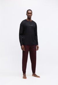 Schwarzes Langarmshirt mit "HUGO"-Logo auf der Vorderseite, kombiniert mit roten karierter Hose. Leichte Fabric und lockere Passform.