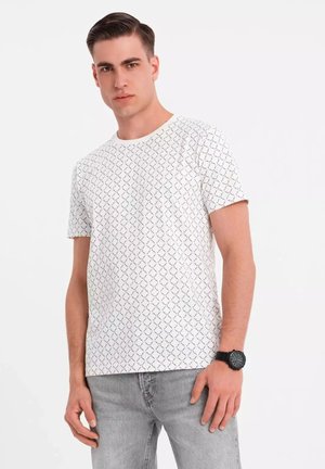 Hvid kortærmet t-shirt med et geometrisk sort mønster. Rund halsudskæring, letvægtsstof, parret med grå jeans og et sort ur.