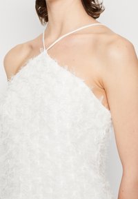 Bílé šaty s texturovanou, peříčkovou tkaninou, nastavitelné tenké ramínka a přiléhavý střih. Obsahují design s jedním ramínkem a jemný lesk.