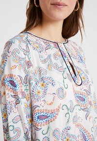 Flerfärgad blus med blommig paisley-mönster, lättviktsmaterial, rund halsringning och kontrasterande foder som omger halsringningen.