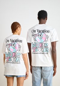 T-shirts de algodão brancos com um gráfico de desenho animado colorido nas costas com o texto "Em Férias - Tour Mundial" e detalhes em rosa e azul.